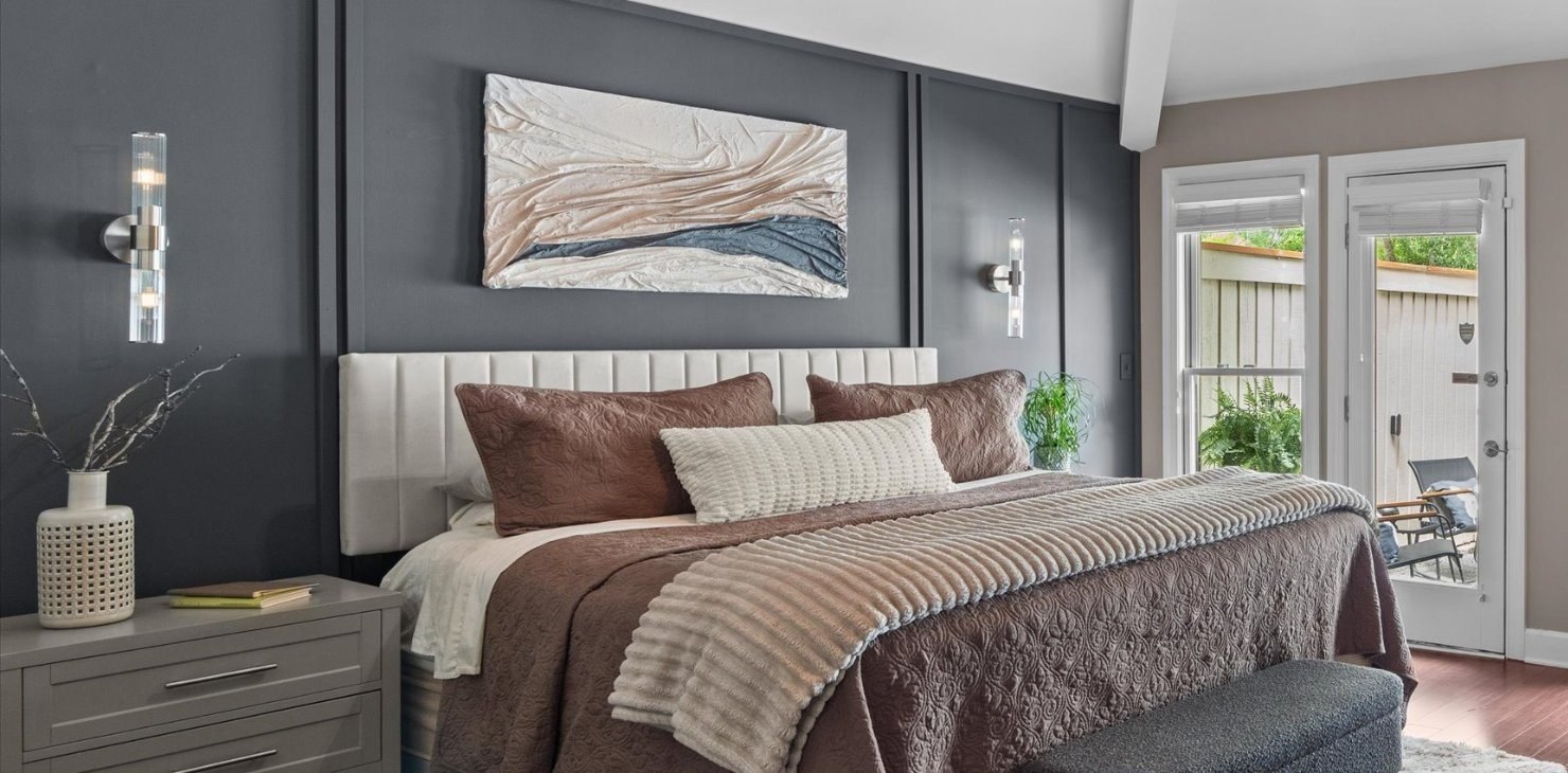 A cream, blush and slate textured relief installed above an upholstered bed against a charcoal paneled wall